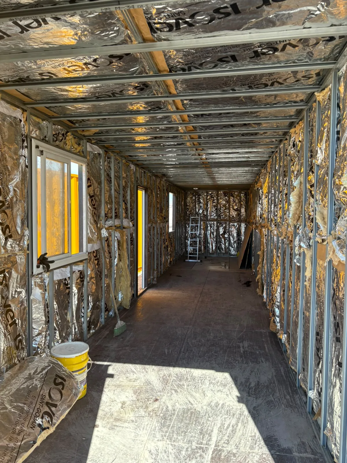Interior de obra con aislación y perfilería, con ventanas y una escalera al fondo